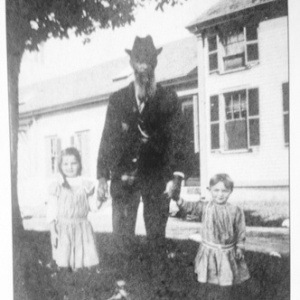 Jonathan Peaslee Little stands with his two grandchildren, Helen and Jewell Woodsom, at the family farm in Amesbury, MA.  ca. 1910's